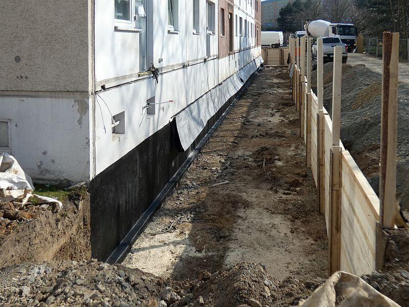 Das Bild zeigt eine schwarz gestrichene Kellerwand. Das dient der Abdichtung gegen Wasser. Jetzt wird hier ein Fundament gebaut.