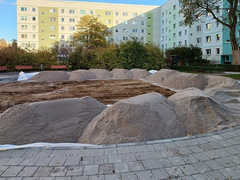 Das Bild zeigt einen Spielplatz. Es sind viele Sandhaufen zu sehen. Der Spieleplatz ins in einer Grünanlage. Um die Grünanlage stehen Miethäuser. Das ganze Viertel nennt sich Regenbogenviertel.