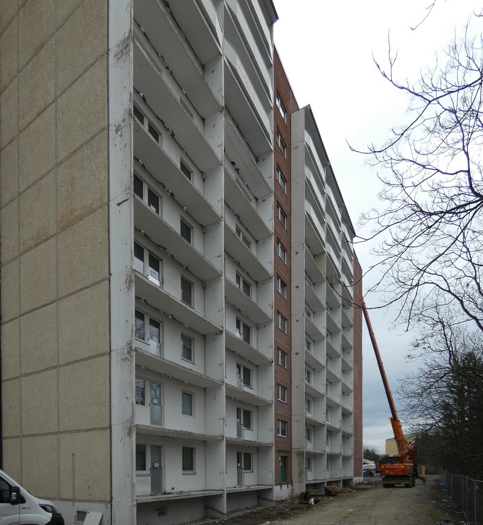 Das Bild zeigt ein Wohnhochhaus. An dem sind die Brüstungen der Balkone demontiert. Im hintergrund ist ein Kran zu sehen, der bei der Demontage unterstützt.
