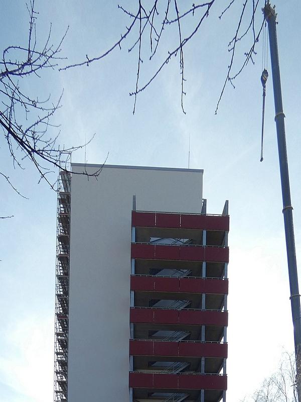 Das Bild zeigt einen Kran. Der Kran hat ein Balkonteil abgesetzt. Der Balkon gehört zu einem Wohnhaus. Das Wohnhaus steht in Leipzig.