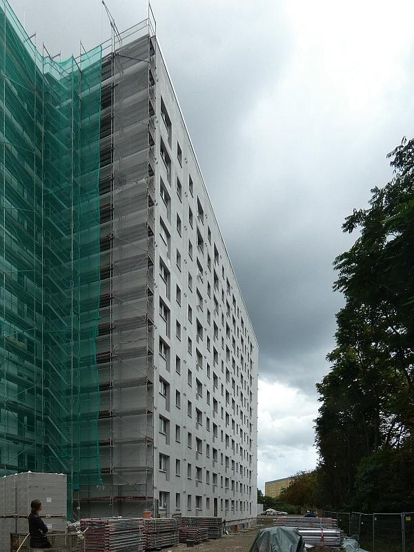 Das Bild zeigt eine Fassade. Die Fassade wurde wärmegedämmt. Die Gerüste an der Fassade wurden abgebaut. Im Vordergrund stehen die Gerüste noch. Das ist ein anderes Haus.