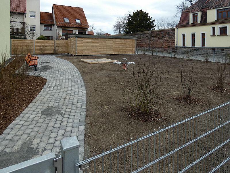 Das Bild zeigt die Außenanlage zu einem neu errichteten Wohnhaus mit Sträuchern, zukünftiger Rasenfläche, Weg und Bänken zum ausruchen.
