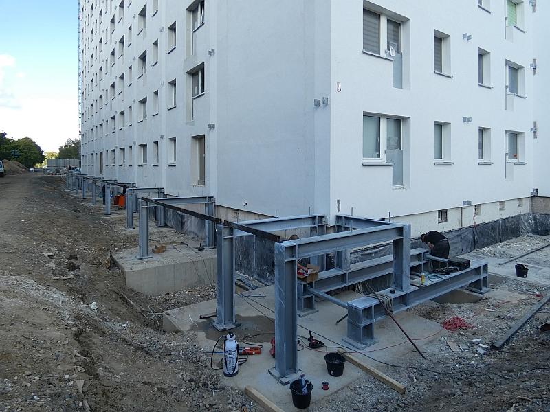 Das Bild zeigt Stahlbau. Es ist die unterste Etage zu sehen. Mit dem Stahlbau werden Balkone gebaut. Die Balkone kommen an ein Wohnhaus. Das Haus befindet sich in Leipzig.