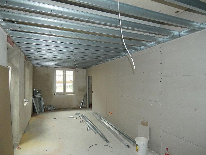 Auf dem Bild sieht man eine Wand aus Trockenbau. Diese teilt die Wohnräume auf. An der Decke sieht man Metallstreben. Diese werden noch verkleidet. So bekommt man eine glatte Untersicht der Decke.