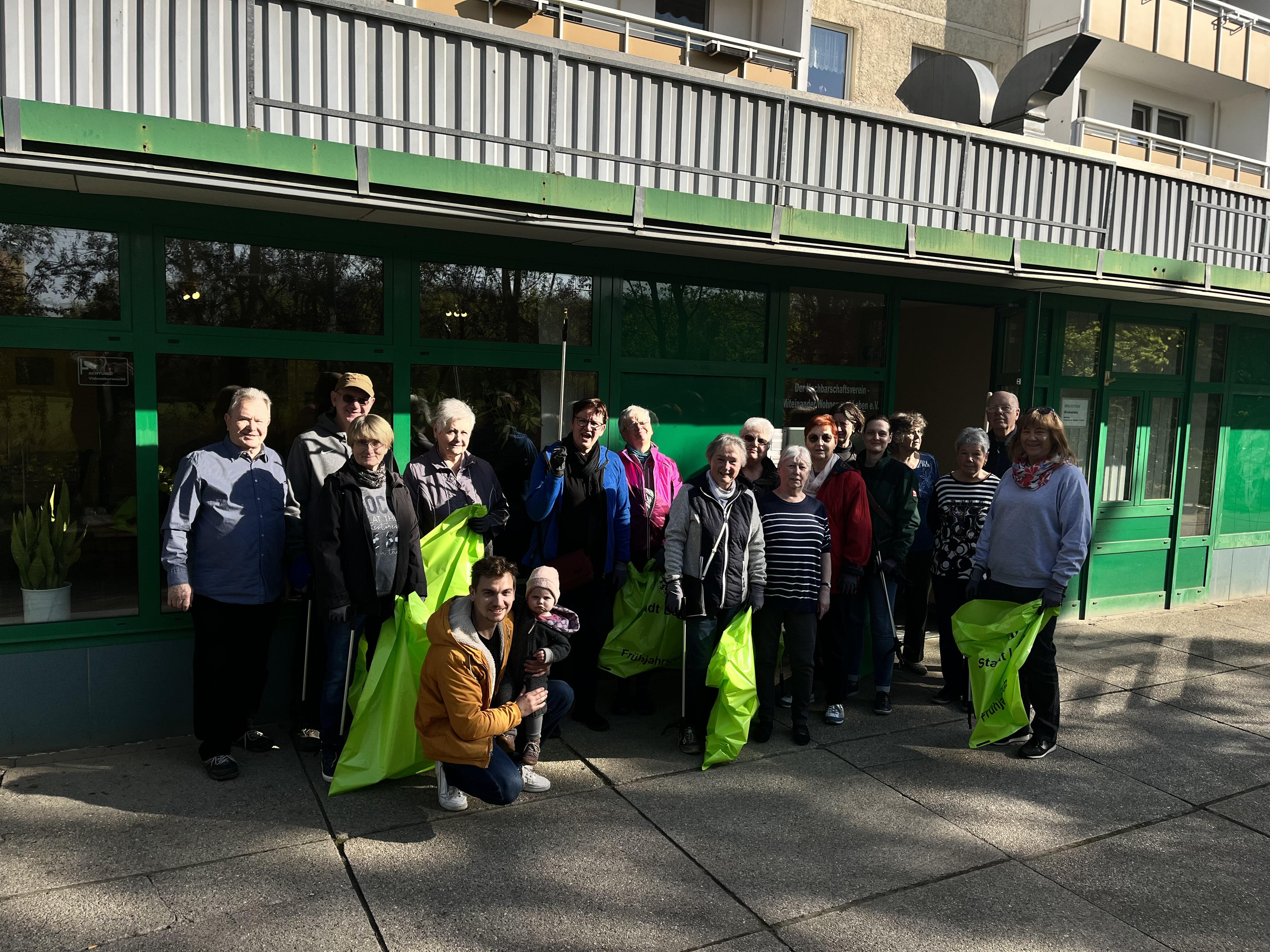 Das Bild zeigt viele Menschen. Die Menschen haben Müllsäcke in der Hand. Die Menschen haben Greifwerkzeuge in der Hand. Die Menschen haben Müll aufgesammelt. Der Müll wurde in Leipzig Grünau-Ost gesammelt. Die Müllsammlung heißt Frühjahrsputz.