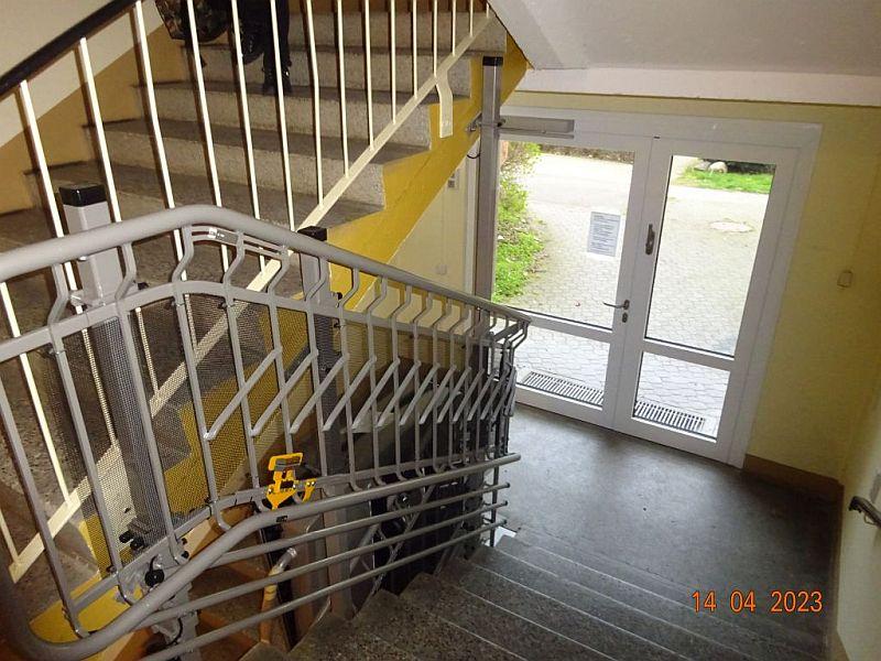 Das Bild zeigt einen Treppenlift. Der Treppenlift geht bis zum Aufzug. Der Treppenlift ist in einem Wohnhaus. Das Wohnhaus steht in Leipzig.