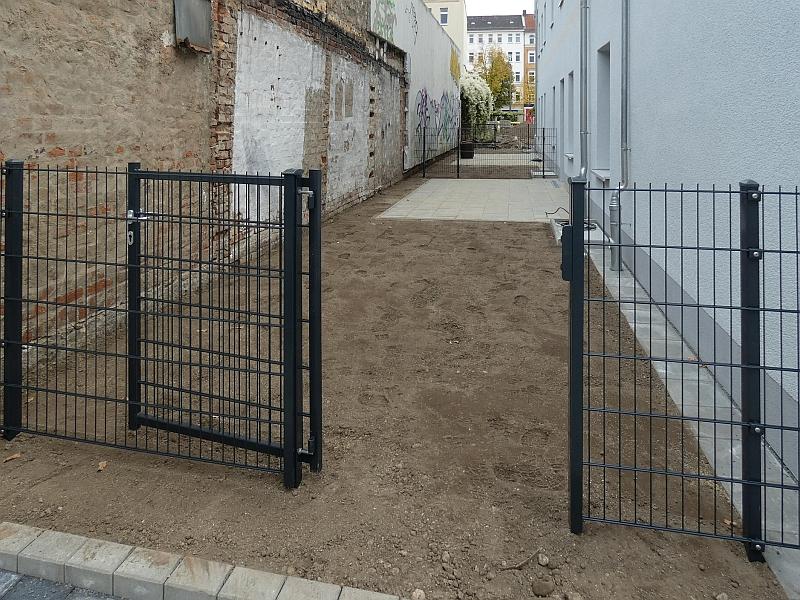 Das Bild zeigt einen Zaun. Hinter dem Zaun sind Terrassen zu erkennen. Die Terrassen gehören zu Wohnungen. Die Wohnungen sind im Erdgeschoss.