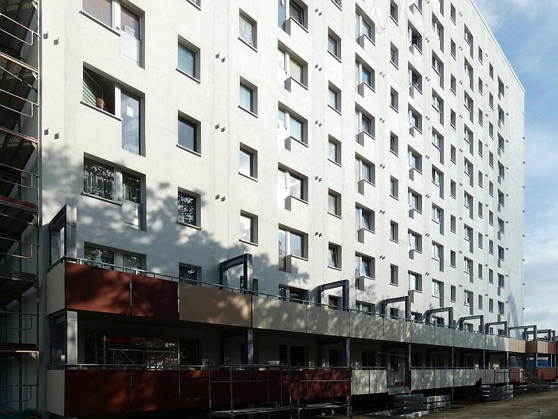Das Bild zeigt ein Wohnhaus. An dem Wohnhaus werden Balkonreihen angebaut. Die Balkone dienen auch als Fluchtweg.. 