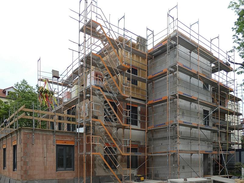 Auf dem Bild sieht man einen Rohbau. Oben links ist ein Richtkranz zu sehen. Es wurde Richtfest gefeiert. Der Rohbau ist fertig.