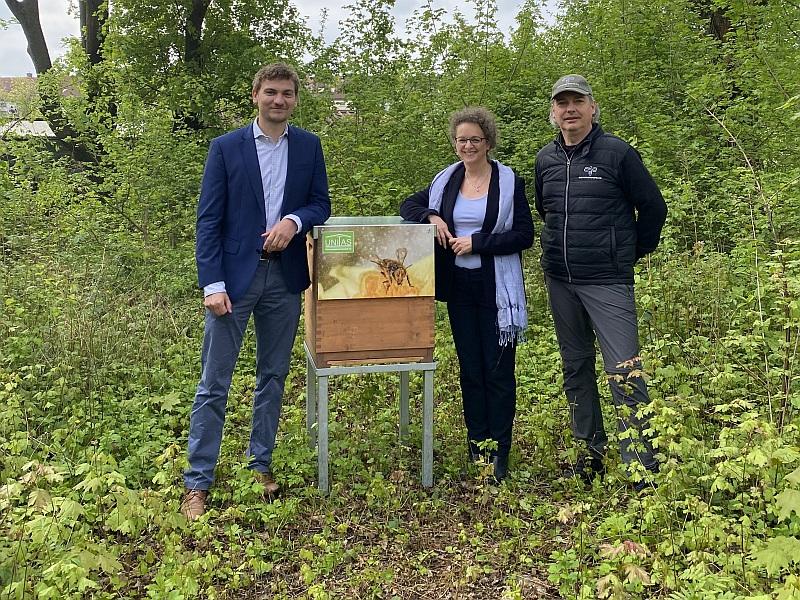 Auf dem Bild sieht man einen Bienenstock und drei Leute. Die haben den Bienenstock einem Garten aufgestellt. Der Honig sollen die Bewohner bekommen.