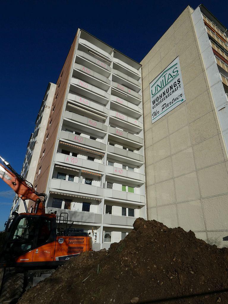 Blick auf ein elfgeschossiges Wohnhochhaus mit einem Backer im Vordergrund. Weiterleitung auf den Baustellenticker.