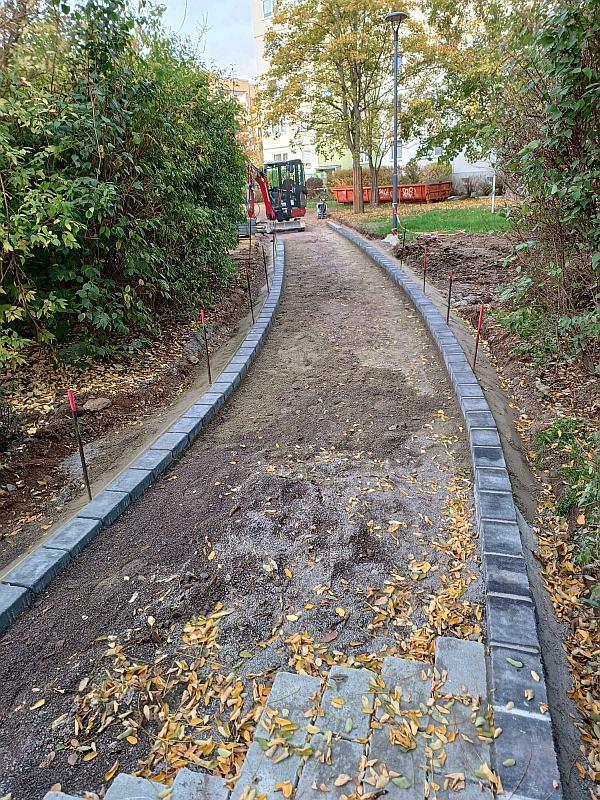 Das Bild zeigt einen Weg im Bau. Der Weg gehört zu einer neu gestalteten Grünanlage. Um die Grünanlage stehen Wohnhäuser. In den Wohnhäusern gibt es Mietwohnungen. Dies Häuser stehen in Leipzig Lausen-Grünau. Die Grünanlage und die Häuser nennen sich Regenbogenviertel.