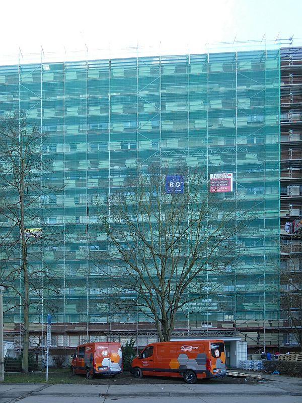 Auf dem Bild ist ein eingerüstetes und mit Planen verhangenes Wohnhochhaus zu sehen, andem klimaschutztechnische Verbesserungen durch Wärmedämmung vorgenommen werden.