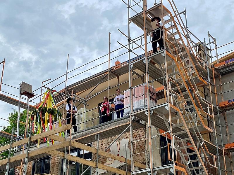 Auf dem Bild sieht man einen Redner. Er hält eine Rede zum Richtfest. Ein Haus wurde im Rohbau fertiggestellt. Das wird gefeiert.